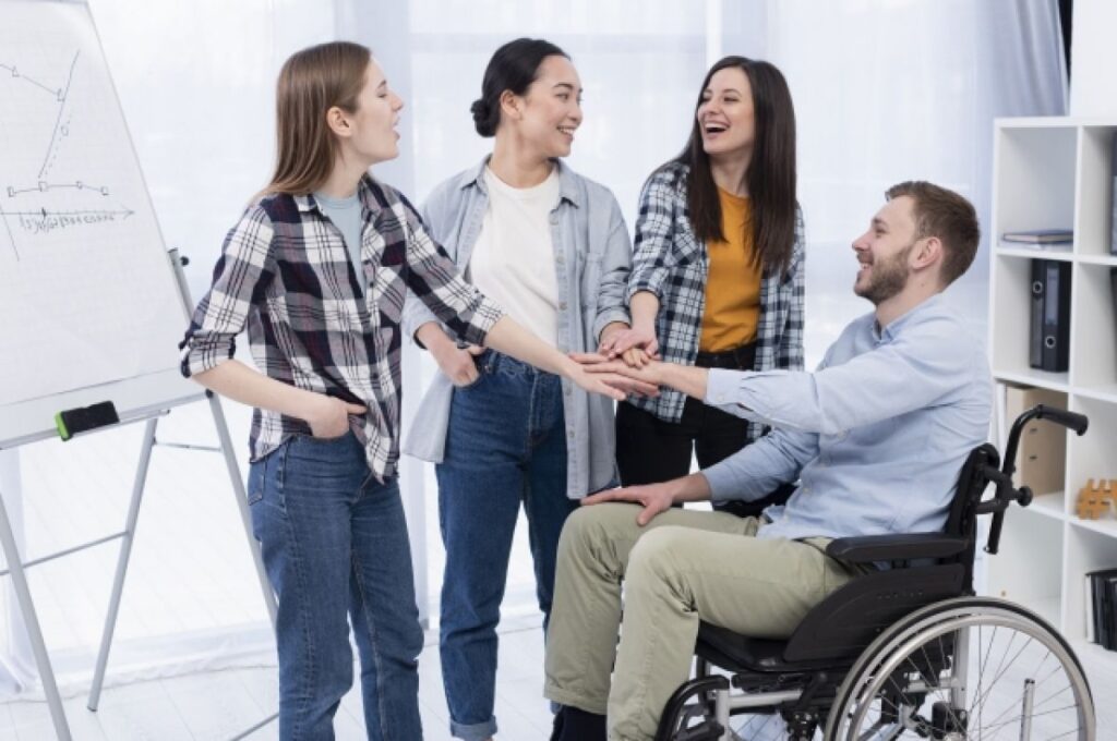 A group of people standing around a man in a wheelchair, shaking his hand and welcoming him into the business office. 