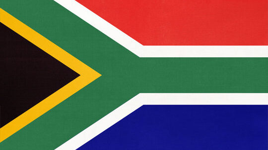 The South Africa flag featuring a black triangle on the left, bordered by yellow and a green capital Y-shape, lying towards the left, bordered by white, with red at the top and blue at the bottom.